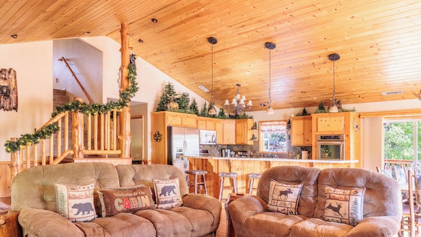 A cozy cabin interior with two plush sofas, a wooden staircase, and a kitchen area.