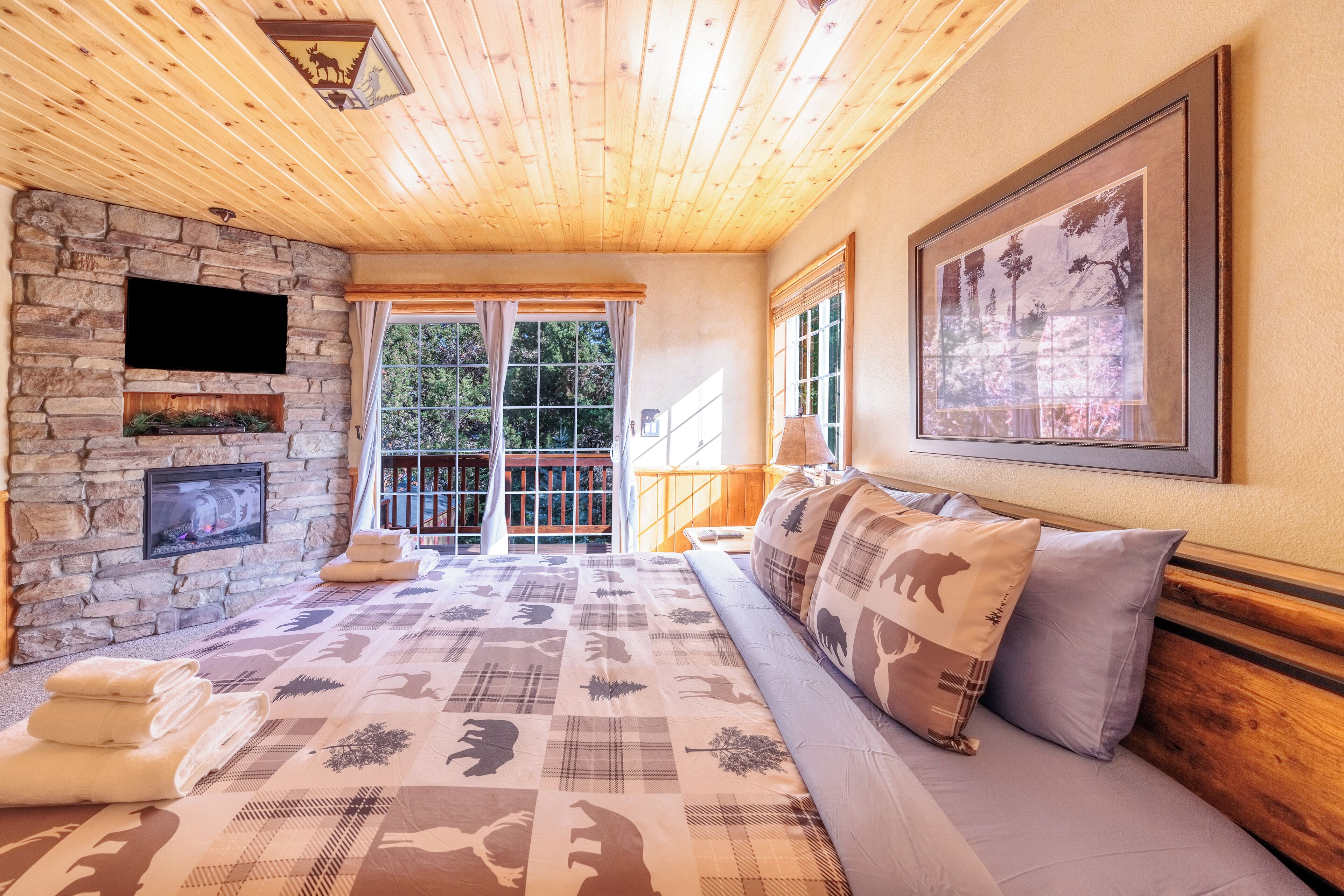 Um quarto aconchegante com lareira de pedra, uma cama grande com roupa de cama estampada, teto de madeira e um quadro na parede.