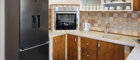 A compact kitchen with a stainless steel refrigerator, a built-in oven, wooden cabinets, and a tiled backsplash.