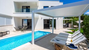 Een modern huis met een zwembad, buitenmeubels en een overdekt terras.