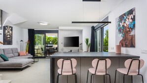 Een moderne woonkamer met een grijze bank, een flatscreen-televisie en een barruimte met drie roze stoelen.