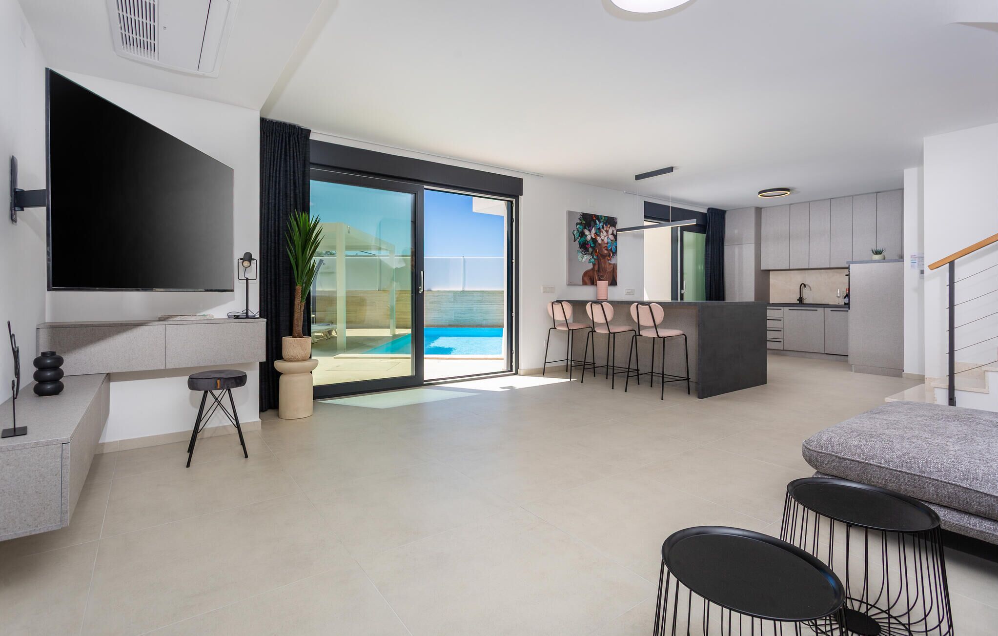 A modern living room with a large TV, a sofa, and a dining area with chairs.