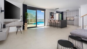 Een moderne woonkamer met een grote televisie, een bank en een eethoek met stoelen.