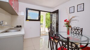 Una cocina moderna con un lavamanos, un comedor con una mesa de vidrio y sillas de metal, y vistas a zonas verdes.