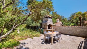Un patio al aire libre con un horno de piedra, una mesa con sillas y un muro de piedra.