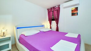 Un dormitorio con cama, mesita de noche, equipo de aire acondicionado y ventana con cortinas.
