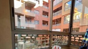A balcony with a white table and chairs, a glass partition, and a view of multi-story buildings. - Secure residence with pool & fiber (Marrakesh)