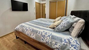 A bedroom with a bed, a TV mounted on the wall, wooden doors, and a black headboard. - Secure residence with pool & fiber (Marrakesh)
