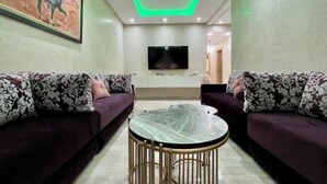 A modern living room with two sofas, a round table, and a flat-screen TV mounted on the wall. - Secure residence with pool & fiber (Marrakesh)