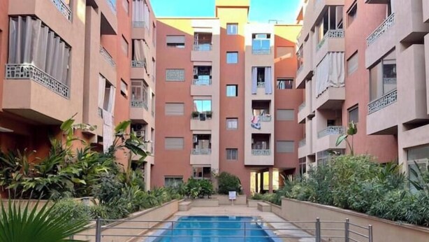 A multi-story residential building with a central swimming pool surrounded by balconies and greenery. - Secure residence with pool & fiber (Marrakesh)