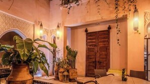 A cozy indoor dining area with a round table and chairs, surrounded by potted plants and a decorative pool. - Riad MAYAN : Heated Pool & GYM (Marrakesh)