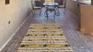 A covered corridor with a patterned floor, a table and chairs, and a hanging light fixture. - Skoura Ranch - Palmeraie (Skoura)