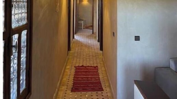 A narrow hallway with a patterned carpet, a wooden ceiling, and a wall-mounted light fixture. - Skoura Ranch - Palmeraie (Skoura)