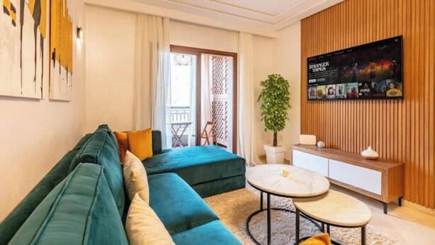 A modern living room with a teal sofa, a round coffee table, and a TV on the wall.