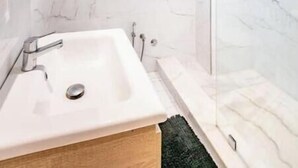 A modern bathroom with a marble wall, a white sink, and a glass shower enclosure.