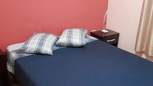 A room with a bed, two bedside tables, a nightstand, and a lamp.