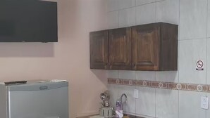 A kitchen with a microwave, cabinets, a sink, and a television mounted on the wall.