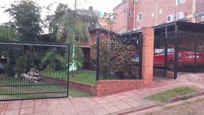 A gated parking area with a red car inside, surrounded by a brick wall and a metal fence.