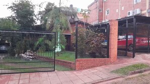 Uma área de estacionamento fechada por portão, com um carro vermelho no interior, cercada por uma parede de tijolos e uma cerca de metal.