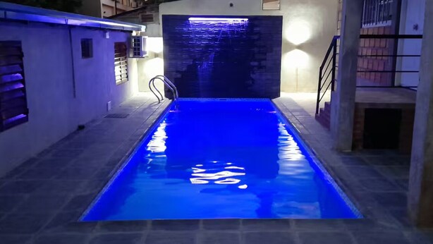 Uma piscina iluminada em azul, uma parede de pedra e uma escadaria.