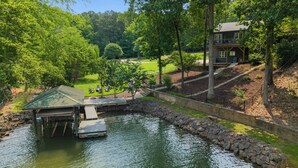 A lakeside property with a dock, a house, and a well-maintained lawn. - Cove's End by Avantstay Dock, Game Room, Fire Pit & Forest Views (Mooresville)