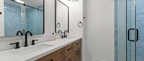 A bathroom with a white vanity, black faucets, a large mirror, and a glass shower enclosure.