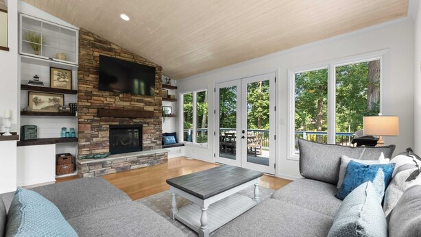 A living room with a stone fireplace, a large window, and a sofa. - Cove's End by Avantstay Dock, Game Room, Fire Pit & Forest Views (Mooresville)