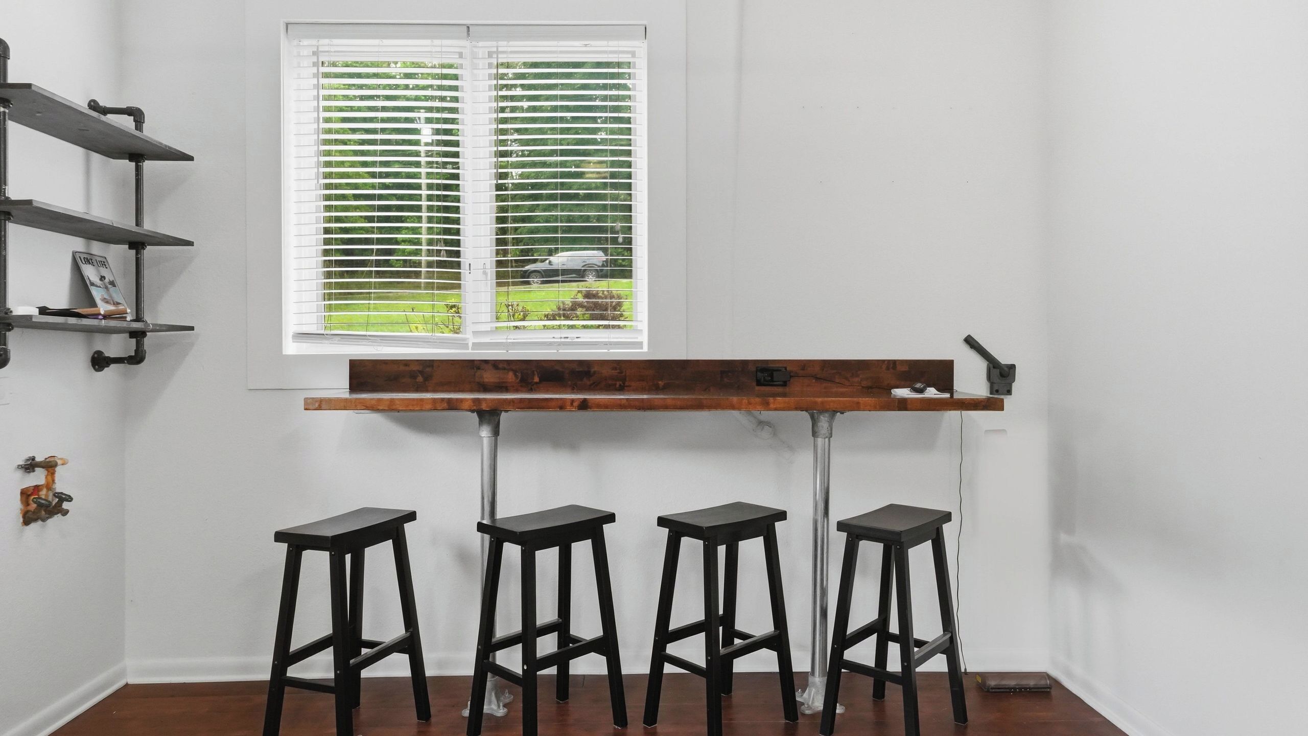A room with a window, a wooden bar counter, and four stools.