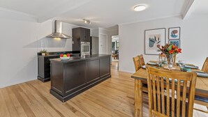 A modern kitchen with dark cabinetry, a central island, and a dining area with wooden chairs and a table. - Family Fun Haven (Taupo)