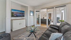 A modern living room with a glass coffee table, a black leather sofa, and a large flat-screen TV mounted on the wall. - Family Fun Haven (Taupo)