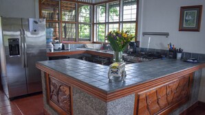 A kitchen with a large island, a refrigerator, a water dispenser, and a window with a view of trees. - "Stalley House" Beachfront, 6bd, Pool, Maid, Cook, SUV's, 7 Kayaks (Jaco)