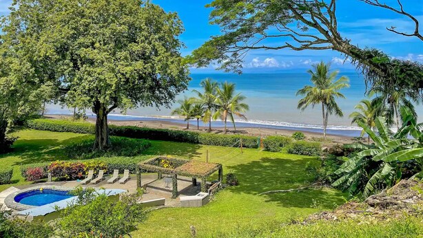 A lush garden with a swimming pool, palm trees, and a view of the beach. - "Stalley House" Beachfront, 6bd, Pool, Maid, Cook, SUV's, 7 Kayaks (Jaco)