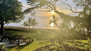 A serene outdoor area with a seating arrangement overlooking a beach, palm trees, and a sunset. - "Stalley House" Beachfront, 6bd, Pool, Maid, Cook, SUV's, 7 Kayaks (Jaco)