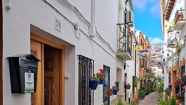 A narrow street lined with white buildings, each with a wooden door and potted plants.