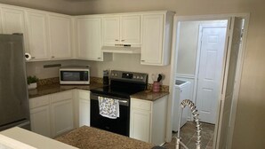A kitchen with white cabinets, a stainless steel refrigerator, a microwave, an oven, and a sink with a modern faucet. - Charming 2-bedroom house in Flowood, Pet Friendly w/Fenced Backyard and Sunroom (Brandon)