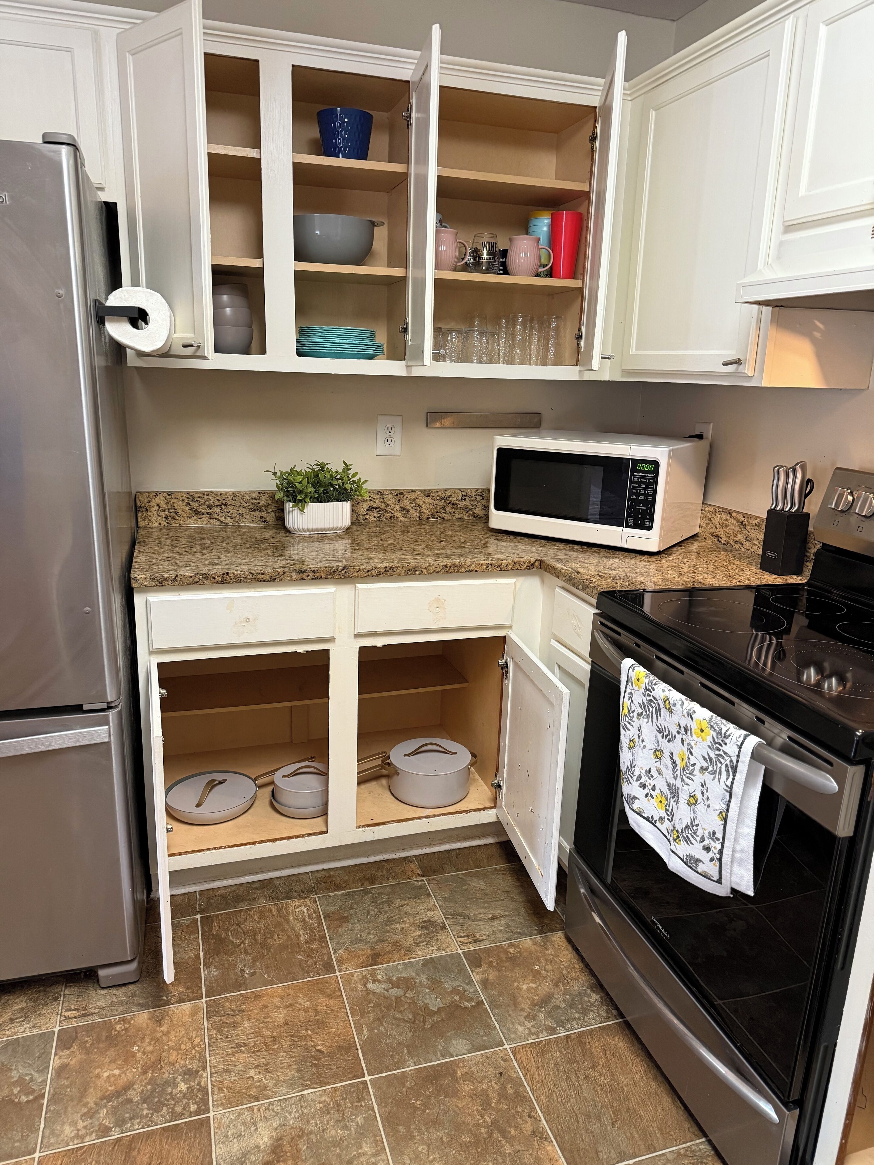 Una cocina con armarios blancos, un refrigerador de acero inoxidable, un microondas, un horno y un lavamanos.