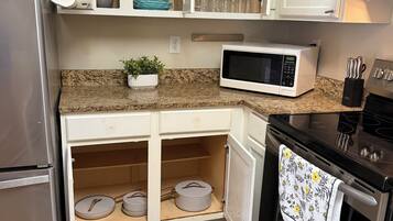 Una cocina con armarios blancos, un refrigerador de acero inoxidable, un microondas, un horno y un lavamanos.