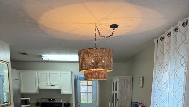 A dining area with a round table, white chairs, and a hanging wicker chandelier. - Charming 2-bedroom house in Flowood, Pet Friendly w/Fenced Backyard and Sunroom (Brandon)