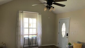 A room with a ceiling fan, a door with a window, a gray sofa with a yellow pillow, and a colorful rug. - Charming 2-bedroom house in Flowood, Pet Friendly w/Fenced Backyard and Sunroom (Brandon)