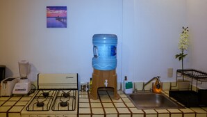 Een keuken met een gasfornuis, een waterdispenser, een spoelbak, een broodrooster en een kleine tafel met een bloevas.
