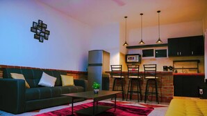 Un salon moderne avec un canapé, une table basse et un tapis rouge. Il y a également un coin cuisine avec un bar et des chaises.