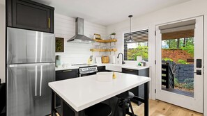 Eine moderne Küche mit Edelstahlgeräten, einer weißen Arbeitsplatte und Blick auf ein bewaldetes Gebiet durch eine Schiebetür.