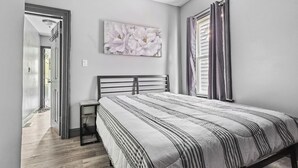 A bedroom with a bed, a bedside table, a wall-mounted artwork, and a window with curtains.