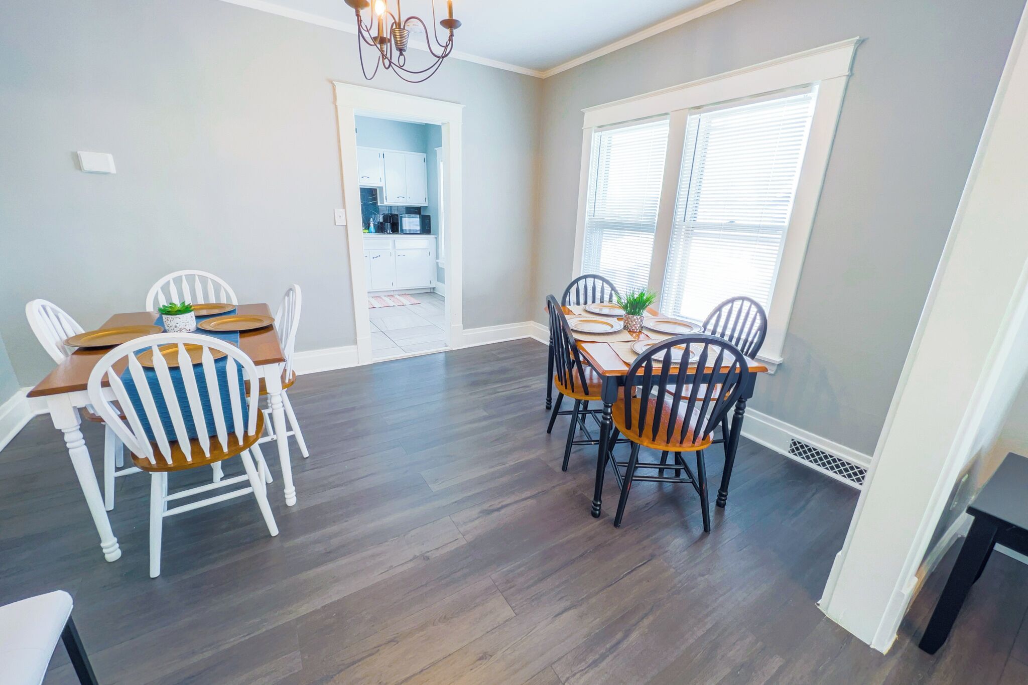 A dining area with a wooden table and chairs, a chandelier, and a view of the kitchen through an open doorway.