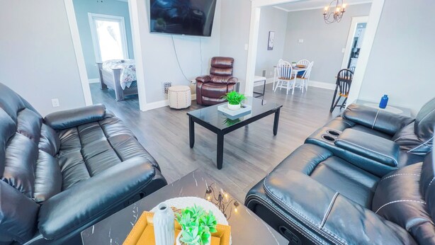 A modern living room with leather sofas, a flat-screen TV, a coffee table, and a dining area with chairs. - Family-Friendly 3Br-Free Parking & Wifi (Niagara Falls)