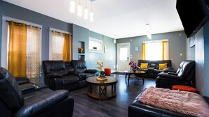 A modern living room with leather sofas, a round coffee table, and a flat-screen TV mounted on the wall. - Double House Rental – 11Br Perfect For Big Groups (Niagara Falls)