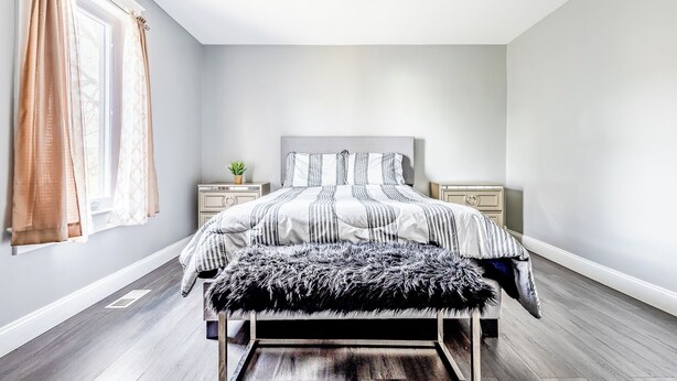 A bedroom with a bed, bedside tables, a ceiling fan, and a window with curtains. - Double House Rental – 11Br Perfect For Big Groups (Niagara Falls)