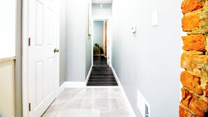 A hallway with a white door on the left, a brick wall on the right, and a staircase in the center leading to another room. - Modern 1Br 1Ba Apartment Close Falls And Casino (Niagara Falls)