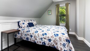 A bedroom with a bed, a nightstand, a window with curtains, and a small framed picture on the wall.