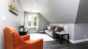 A modern living room with a large window, a sofa, a coffee table, and an orange armchair.